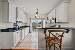 A kitchen with white cabinets, a black countertop, a wooden chair, and a view through a glass door. - 5BR Waterfront Home w/ Pool, hotub, & elevator (North Myrtle Beach)