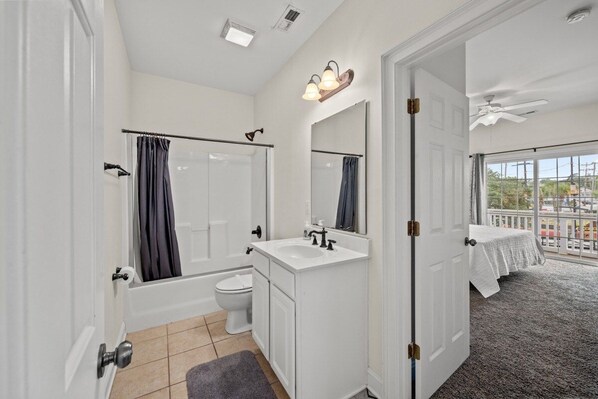 A modern bathroom with a shower, toilet, and sink, featuring a large mirror and a ceiling fan. - 5BR Waterfront Home w/ Pool, hotub, & elevator (North Myrtle Beach)
