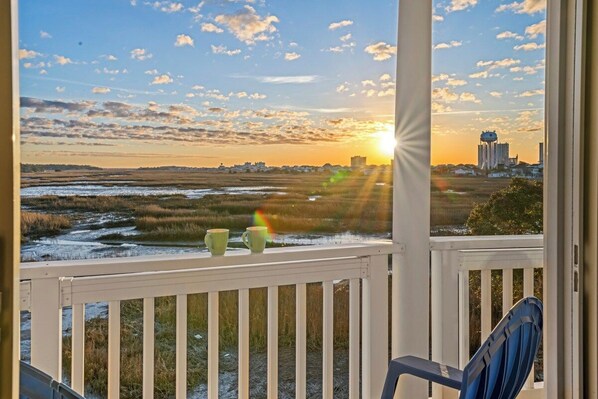 A balcony with a view of a sunset over a marshy landscape and a city skyline. - 5BR Waterfront Home w/ Pool, hotub, & elevator (North Myrtle Beach)