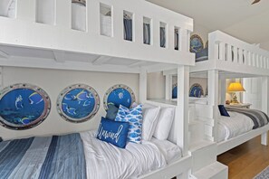 Une chambre avec des lits superposés, décorée sur le thème de la marine, avec des œuvres d'art murales de forme circulaire et un lit recouvert d'une couverture à rayures.