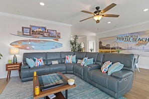 A modern living room with a sectional sofa, a coffee table, and a ceiling fan. - Large Luxury Water Front W/ Pool, HotTub, Elevator (North Myrtle Beach)