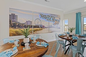 Un coin repas agrémenté d’une grande fresque murale représentant North Myrtle Beach, d’une table en bois dressée pour quatre personnes et de chaises bleu clair.