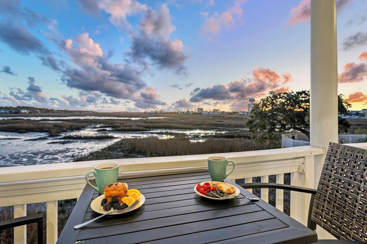 Un balcon avec une table préparée pour le petit-déjeuner, donnant sur un paysage composé d’eau et d’arbres.