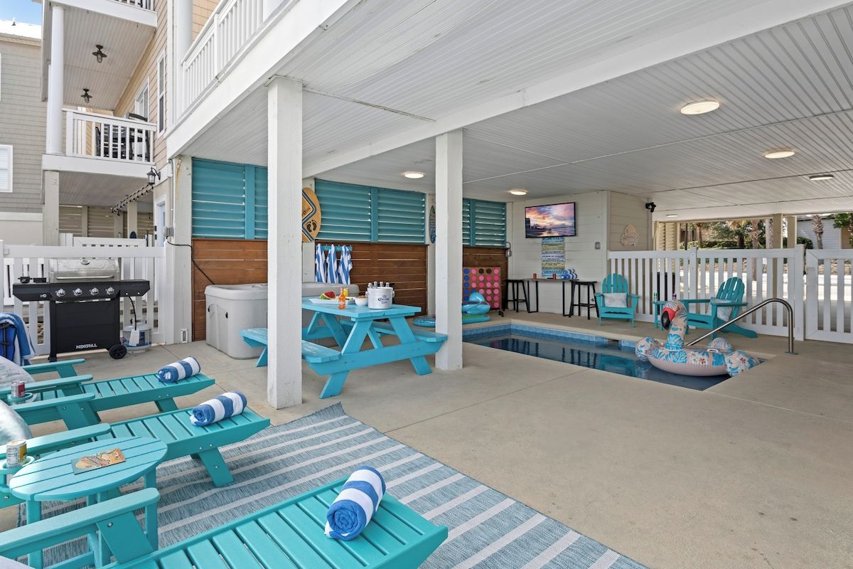 A covered outdoor area with a pool, picnic tables, lounge chairs, and a barbecue grill.