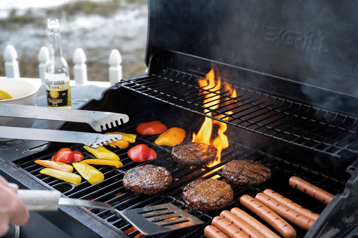 A grill with hamburgers, hot dogs, and vegetables being cooked.
