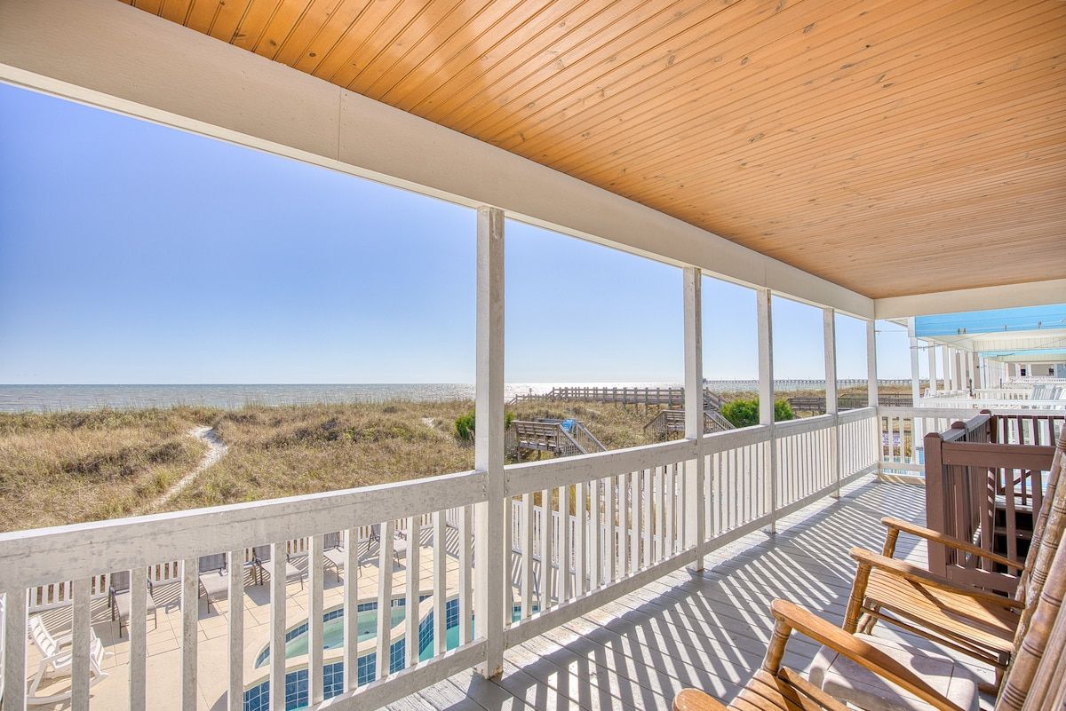 A covered balcony with a view of the beach and ocean.