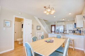 A dining area with a wooden table and blue chairs, a kitchen with white cabinets, and a staircase leading to another level. - 6 BR OceanFront w/ Heated Pool/Hottub Cherry Grove (North Myrtle Beach)