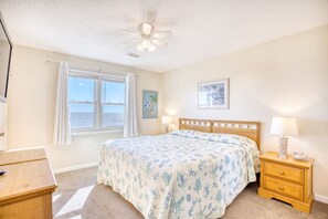 A bedroom with a bed, a nightstand, a desk, a ceiling fan, and a window with curtains.