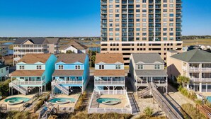 Un quartier résidentiel situé sur la côte, comprenant un grand immeuble à plusieurs étages, plusieurs maisons de plain-pied et un espace piscine.