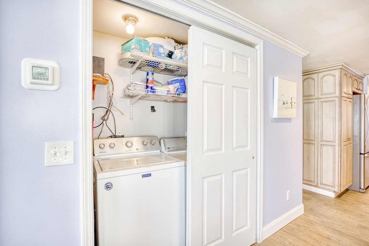 A laundry room with a front-loading washer and dryer, shelves with cleaning supplies, and a door leading to another room.