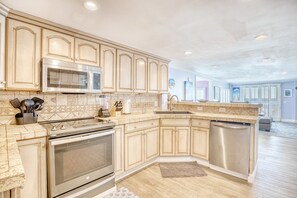 Una cocina con horno empotrado, microondas y lavavajillas, con armarios de madera clara y un salpicadero de azulejos.