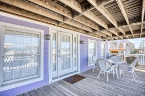 Un porche cubierto con techo de madera, muebles de mimbre blanco y una pared exterior morada.