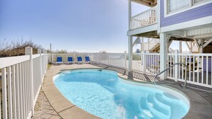 A swimming pool with a white fence, blue chairs, and a multi-level building with balconies. - 52 Week High (North Myrtle Beach)