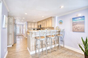 A kitchen with a central island, bar stools, and a view of the adjacent dining area. - Luxury Ocean Front w/ Pool,hotub&basketball court (North Myrtle Beach)