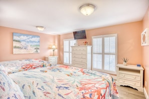 Een slaapkamer met twee bedden, een dressoir, een televisie en een raam met luiken.