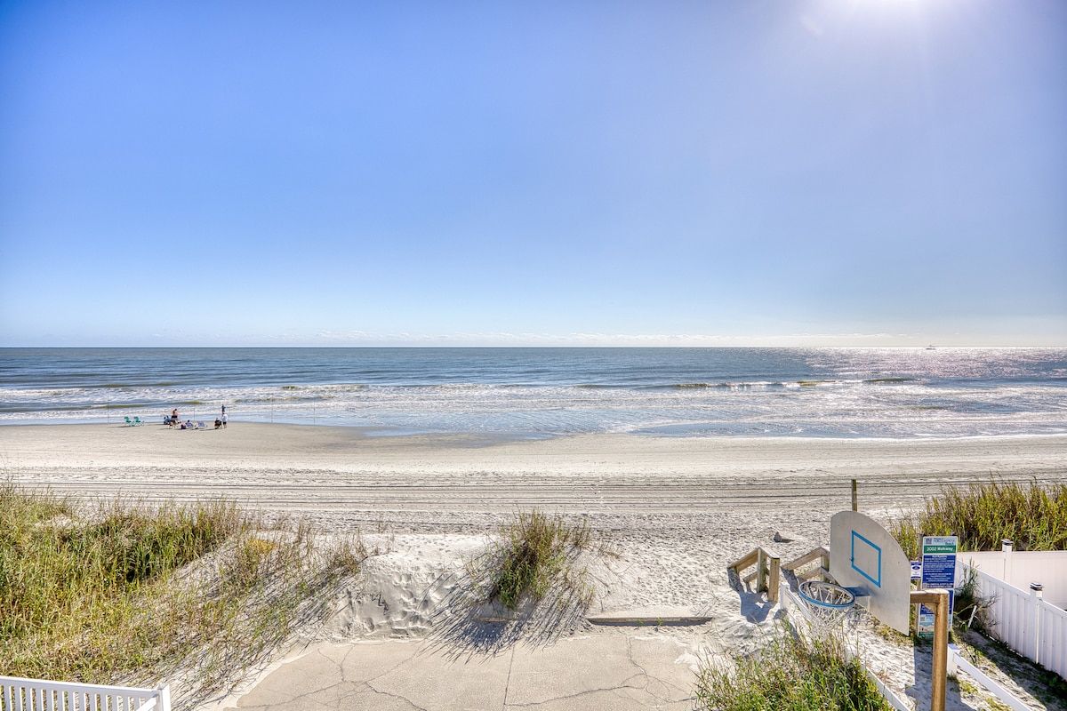 A beach with a basketball court, a fence, and a clear sky.