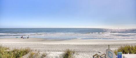 A beach with a basketball court, a fence, and a clear sky.