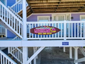 A wooden deck with a sign for Cherry Grove Beachhouses.com, a lower level parking sign, and a staircase.