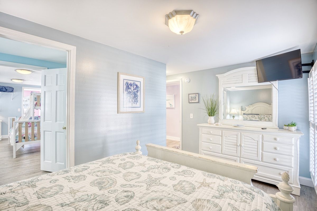 A bedroom with a bed, dresser, and a television mounted on the wall.