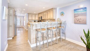 A kitchen with a central island, bar stools, and a view of the adjacent dining area. - 52 Week High (North Myrtle Beach)