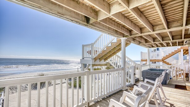 A wooden deck with white railings overlooking the beach, a hot tub, and a staircase leading to an upper level. - 52 Week High (North Myrtle Beach)