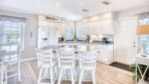 A modern kitchen with white cabinetry, a central island with bar stools, and a built-in refrigerator. - 5 O'Clock Poolside (North Myrtle Beach)