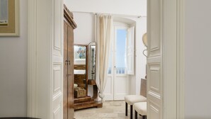 Ein Flur mit einer Holztreppe, die zu einer Tür mit Meerblick führt. An der Wand hängt ein Spiegel und es steht ein kleiner Tisch mit einem Stuhl davor.
