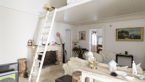 Ein Zimmer mit einer weißen Leiter, einem Kamin, einer Couch und einem Tisch mit diversen Gegenständen.