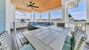 Une terrasse extérieure couverte avec un plafond en bois, un ventilateur de plafond, une table à manger et des meubles en osier.