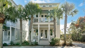 Une maison à deux étages avec un balcon, entourée de palmiers et bordée d’une allée en gravier.