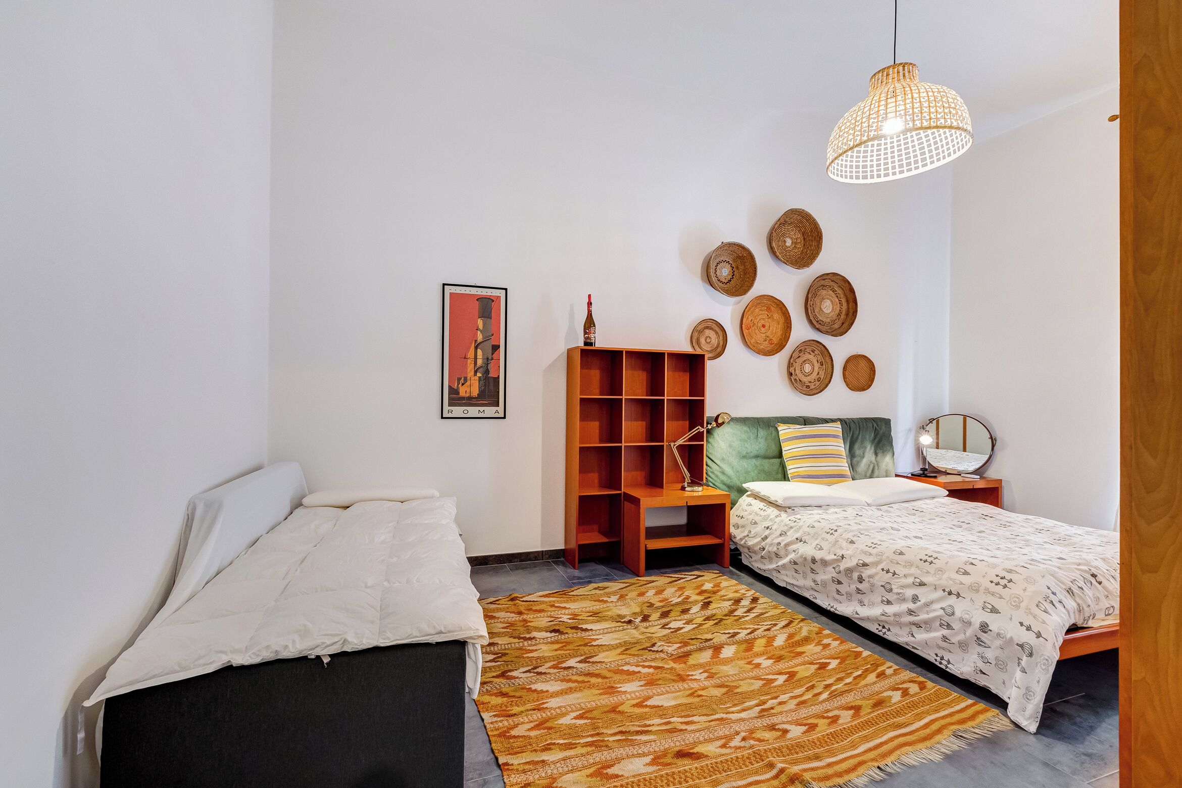 Ein Schlafzimmer mit einem Bett, einem Nachttisch, einem Holzregal, einem gemusterten Teppich und Wanddekorationen.
