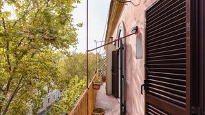A narrow balcony with a wooden railing, potted plants, and a view of a street and trees. - Termini Sweet Home (Rome)