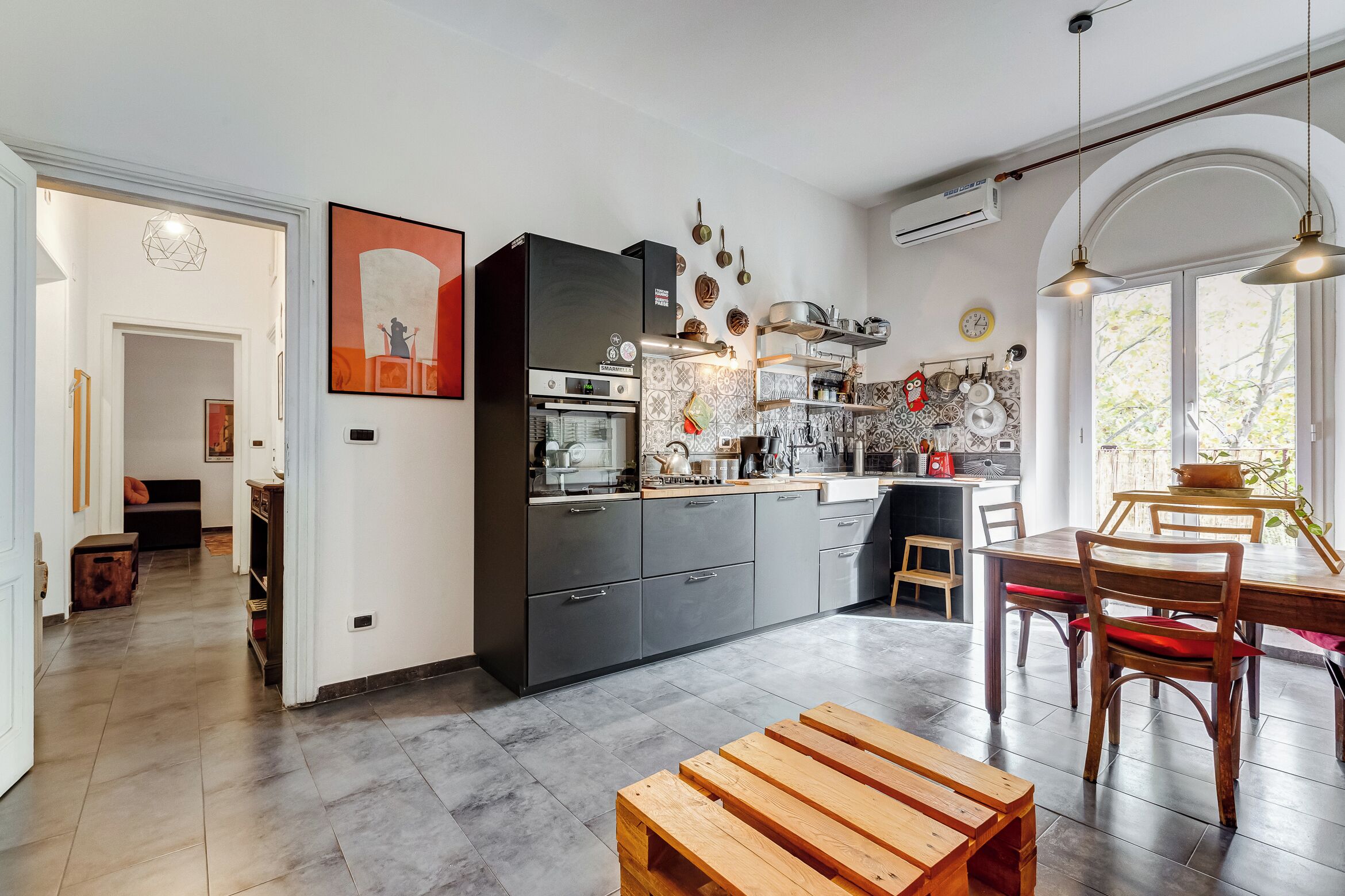 A modern kitchen with dark cabinets, a built-in oven, and a dining area with wooden furniture.
