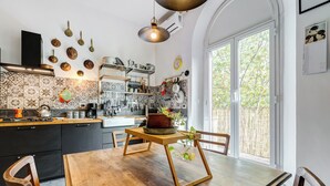 A kitchen with a wooden table and chairs, a hanging pot rack, and a window with a view of trees. - Termini Sweet Home (Rome)