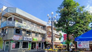 Straßenansicht mit Geschäftsgebäuden, darunter ein Restaurant namens 'Potato Corner' und ein Geschäft namens 'Veeve'. Ein blaues Markisenvorzelt zeigt ein Schild für die Veranstaltung 'Walk & Run for a Cruise'.