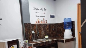 Eine kompakte Küche mit Mikrowelle, Kaffeemaschine und Wasserspender. Ein Schild an der Wand zeigt den Schriftzug: „Mit Liebe gewürzt.“