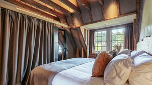A bedroom with a large bed, wooden beams, and a window with curtains.
