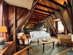 Accogliente camera mansardata con travi a vista in legno, un divano bianco, una sedia di legno e un piccolo tavolo con candele.