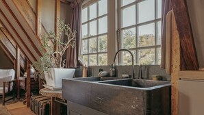 A rustic kitchen with a large sink, wooden beams, and a potted plant.