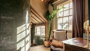 A room with a wooden floor, a large potted plant, a chair, a table, and a window with curtains.