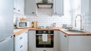 A compact kitchen with white cabinets, a microwave, a stove, and a sink. - Stay Harrogate 3 Bed Holiday Home | Walk to Convention Centre | Parking (North Yorkshire)