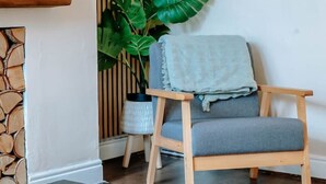 A room with a stone fireplace, a wooden chair, a large plant, and a framed abstract painting on the wall. - Stay Harrogate 3 Bed Holiday Home | Walk to Convention Centre | Parking (North Yorkshire)