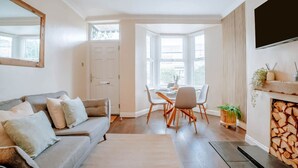 A living room with a sofa, dining table, chairs, a fireplace, and a TV mounted on the wall. - Stay Harrogate 3 Bed Holiday Home | Walk to Convention Centre | Parking (North Yorkshire)