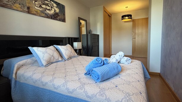 A neatly made bed with a patterned bedspread and pillows, a blue towel, and a rolled-up towel on the bed. - Centrally located apartment in Sarria (Sarria)