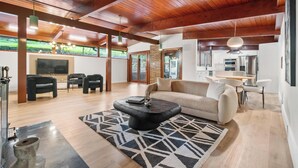A spacious living room with a wooden ceiling, a black coffee table, a beige sofa, and a patterned rug.