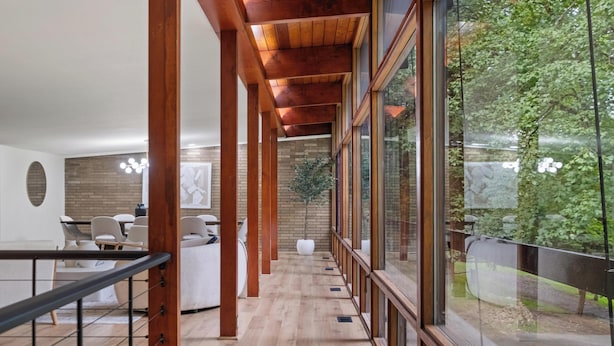 A modern interior with a wooden ceiling, a long corridor, and large windows offering a view of greenery outside.