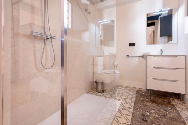 A modern bathroom with a glass-enclosed shower, a toilet, and a vanity with drawers.
