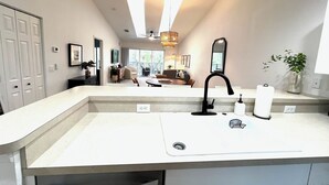 Une salle de bain moderne avec un grand lavabo, un robinet noir et un miroir. Une fenêtre laisse entrer la lumière naturelle et offre une vue sur l’espace de vie.