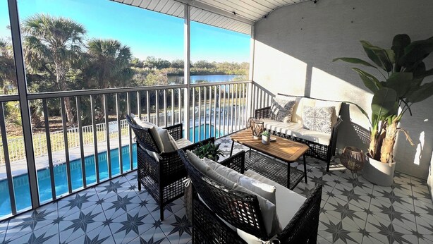 Un balcon donnant sur une piscine et des arbres, aménagé avec des fauteuils et une table en osier.