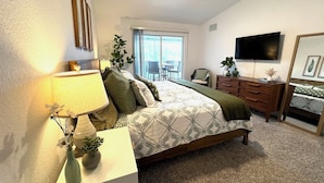 Une chambre à coucher comprenant un lit, un bureau, une chaise, une commode, un téléviseur et un ventilateur de plafond.